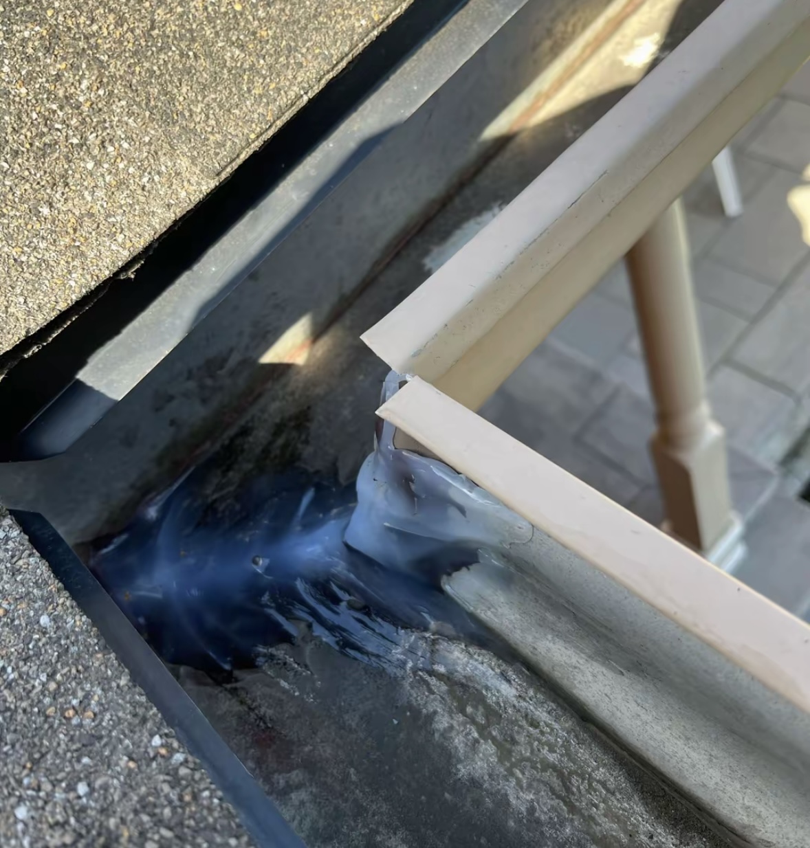 Gutter corner joint freshly sealed with sealant beside a shingled roof