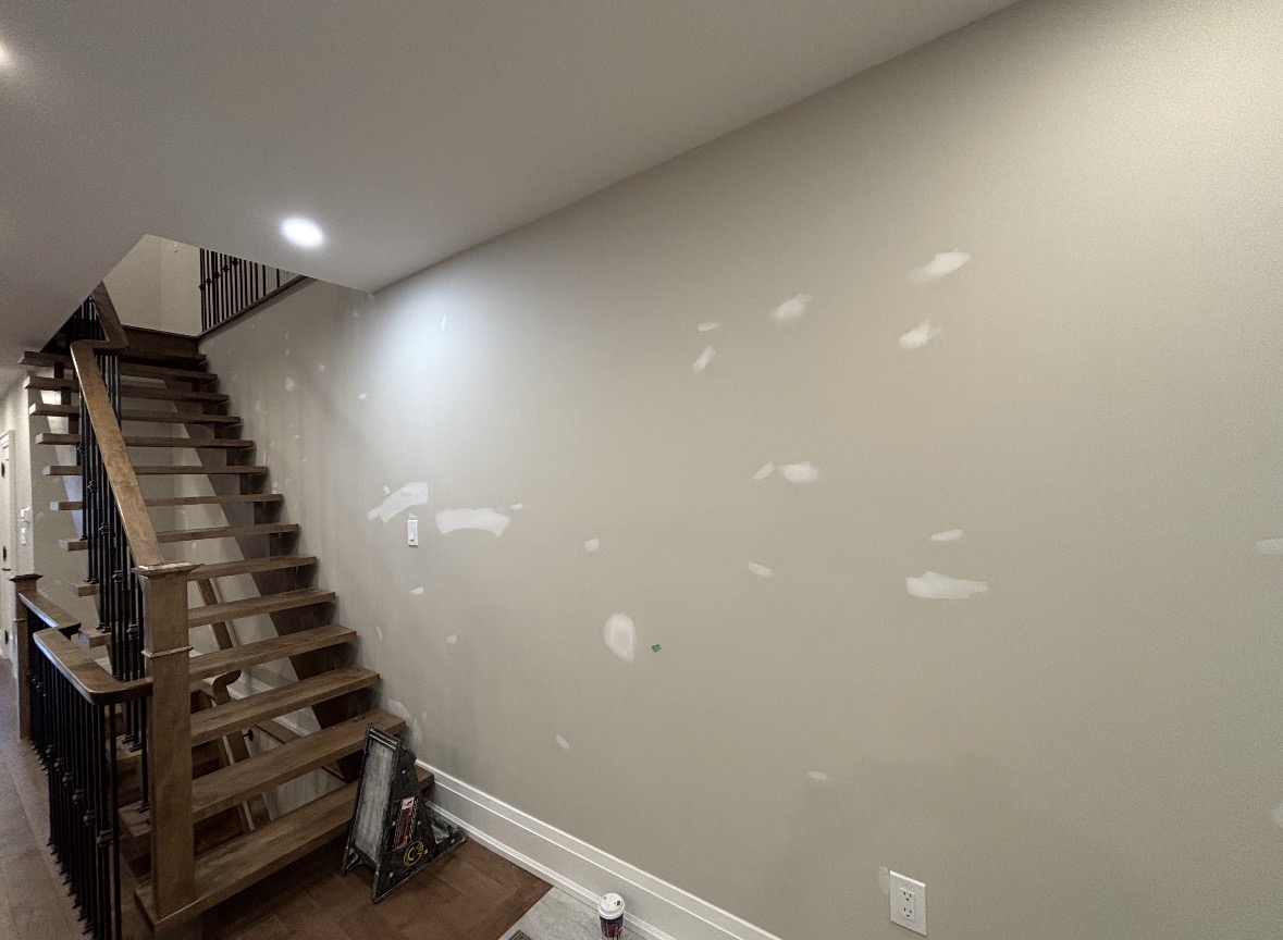 Drywall patched and prepped for painting in a home entryway beside an open-riser wooden staircase