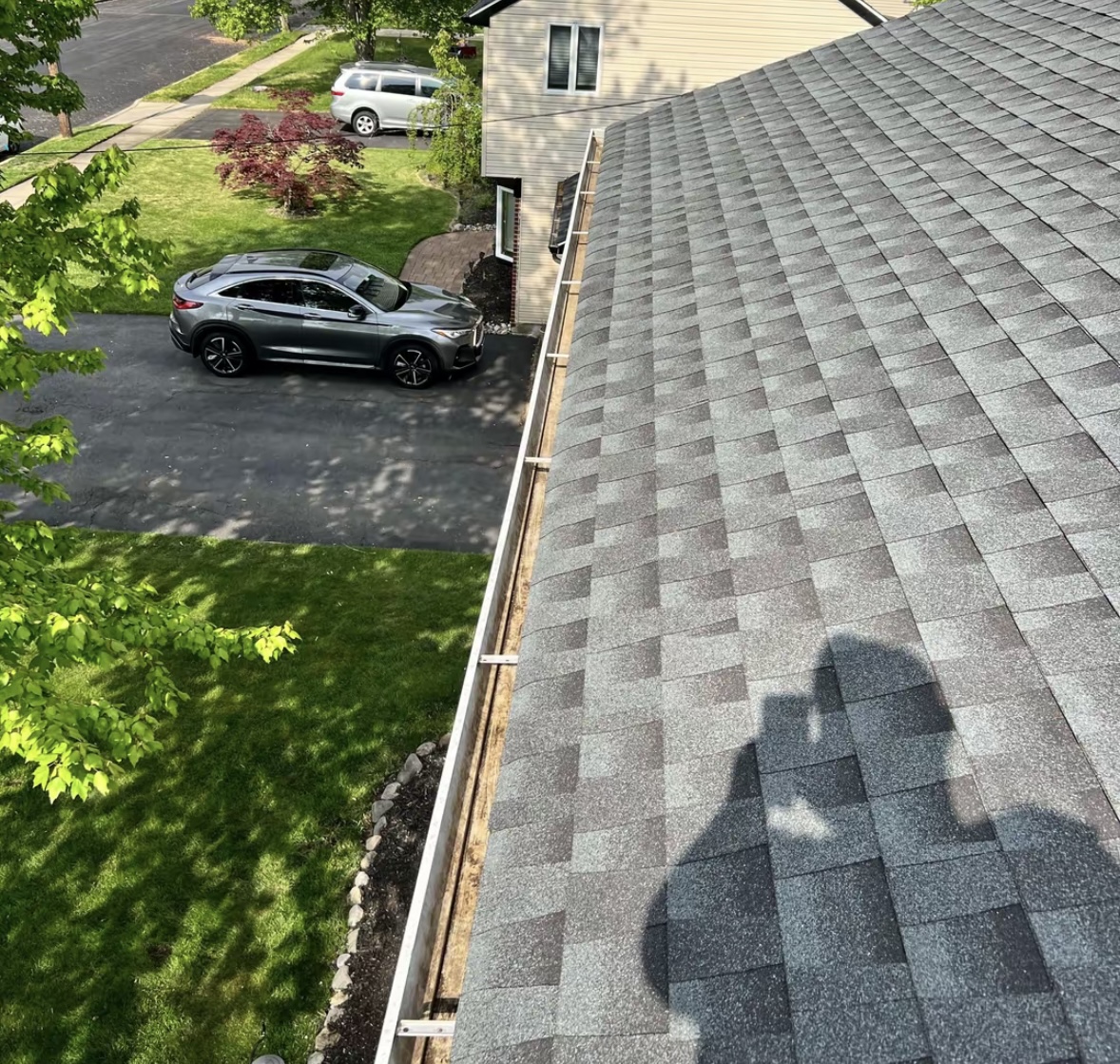 Roofline view along a white gutter with metal hangers beside asphalt shingles