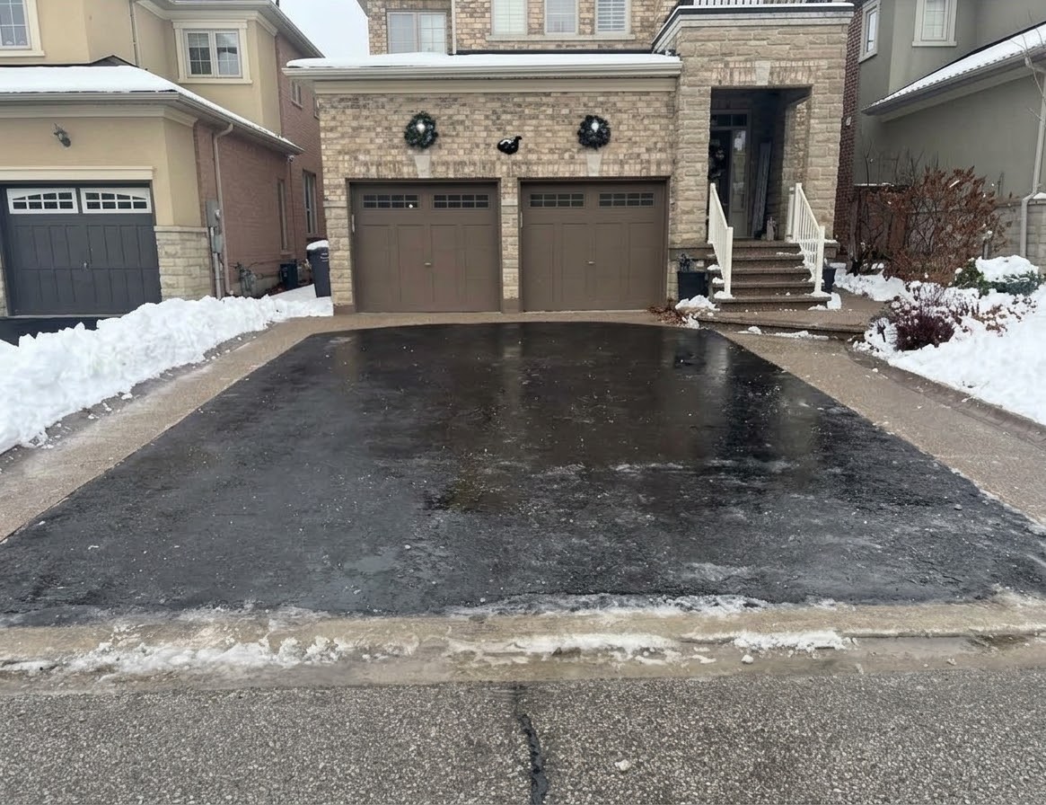 Residential driveway cleared of snow down to the asphalt, with snow banked along both edges of the driveway