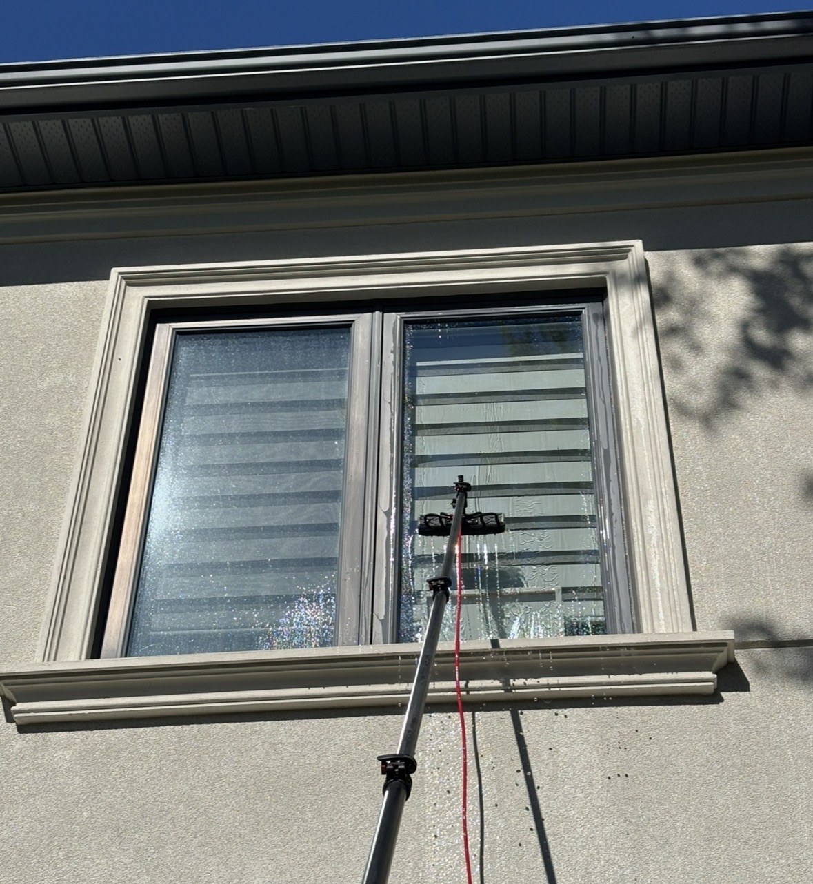 Water-fed pole brush cleaning an exterior window on a stucco home