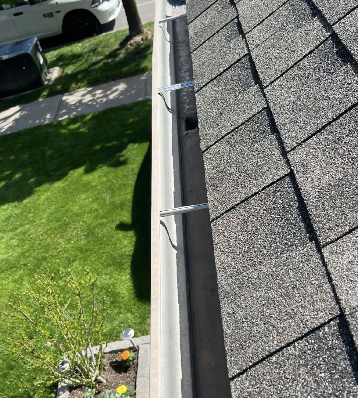 Clean white gutter run along a shingled roof after cleaning