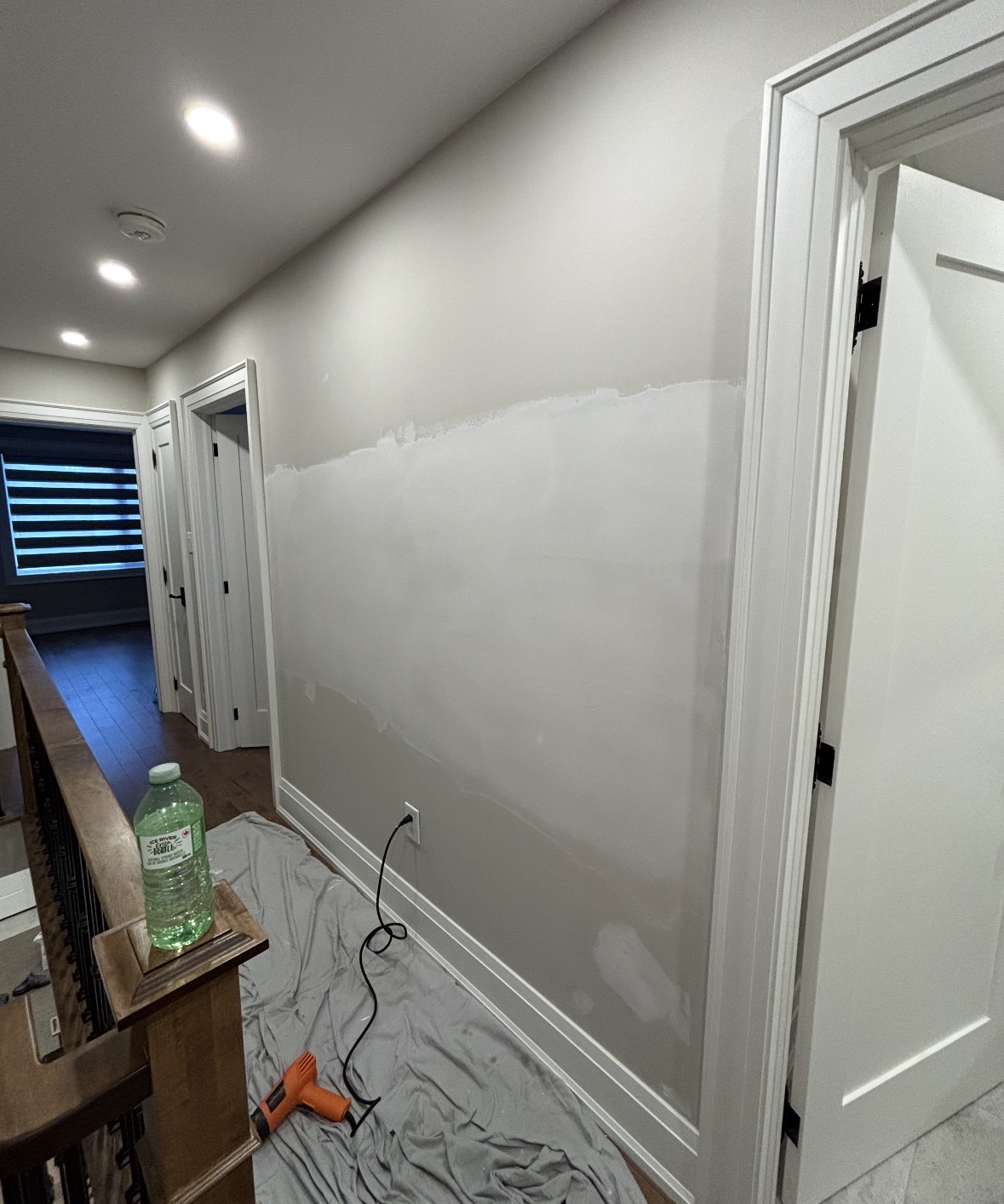 Drywall patching and repair in a residential hallway, with a drop cloth protecting the hardwood floor