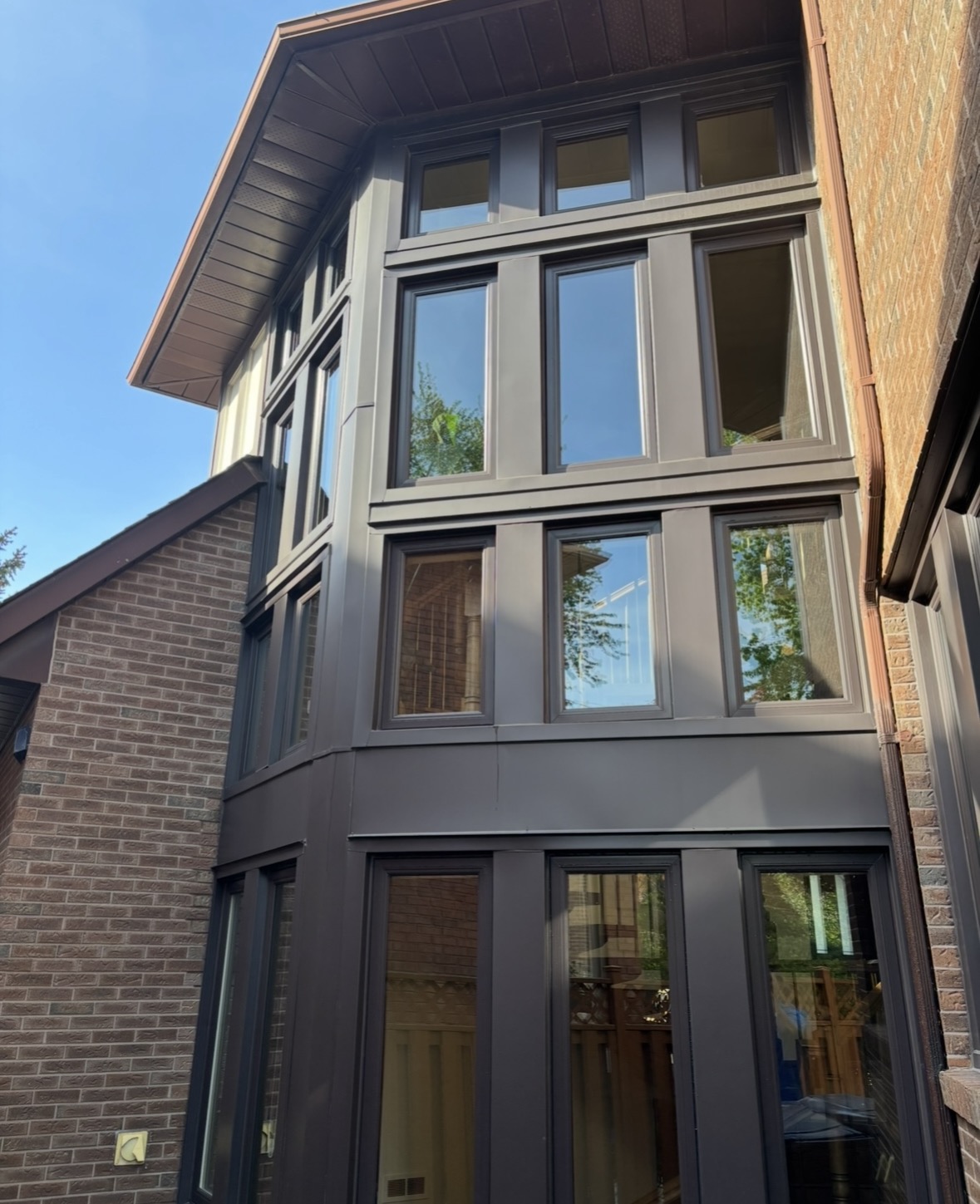 Tall bronze-framed windows on a brick bay tower reflecting trees and sky