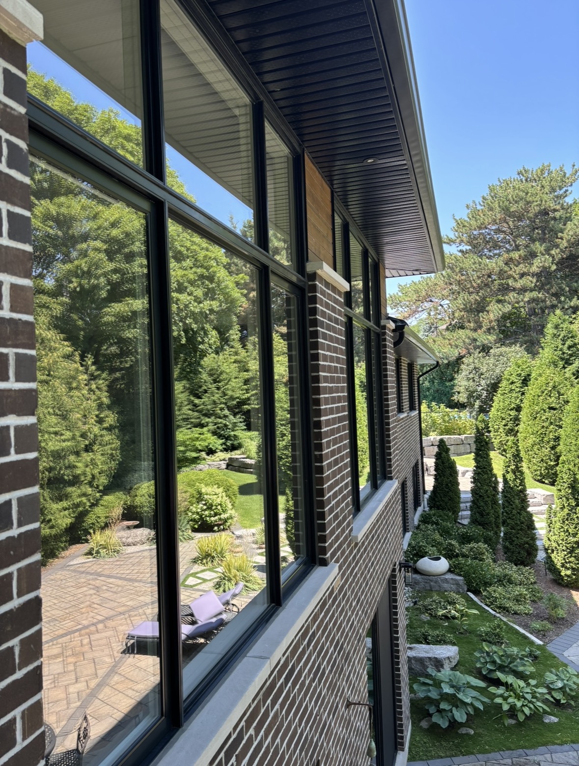 Large black-framed windows along a dark brick home beside a landscaped garden