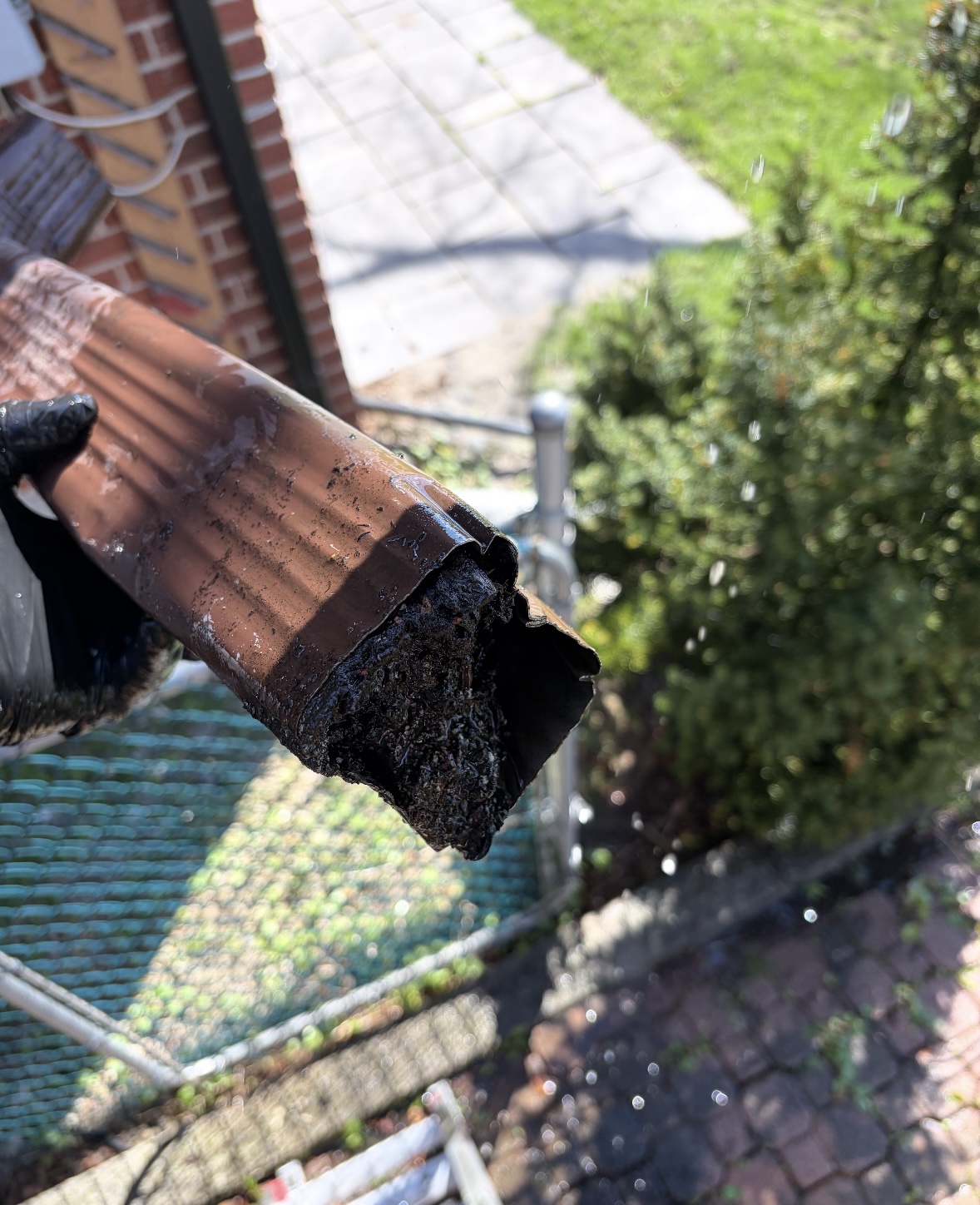 Gutter section held by a technician, caked with dark debris during a cleaning