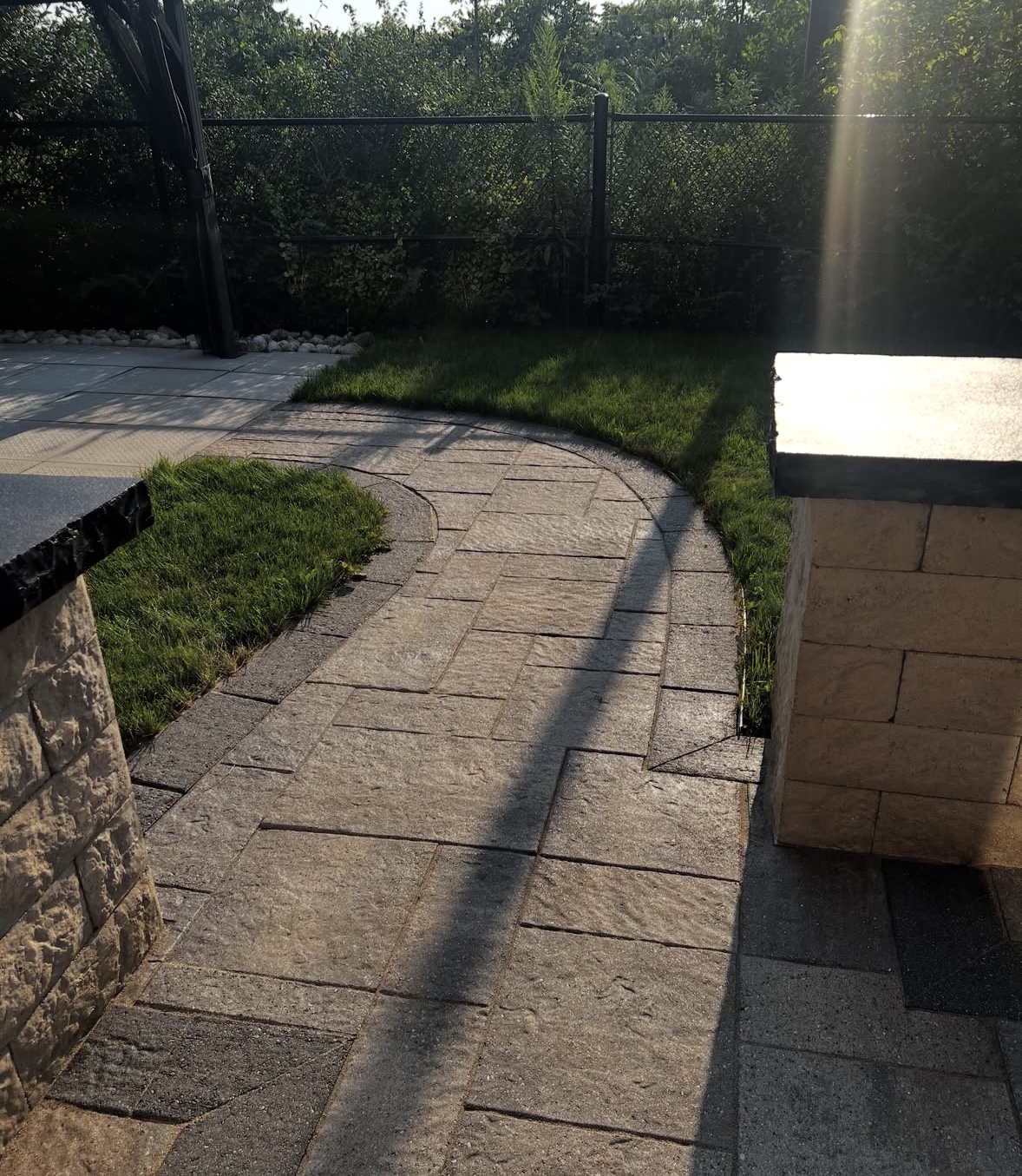 The same curved backyard paver walkway between the two stone pillars, cleaned, sanded and sealed